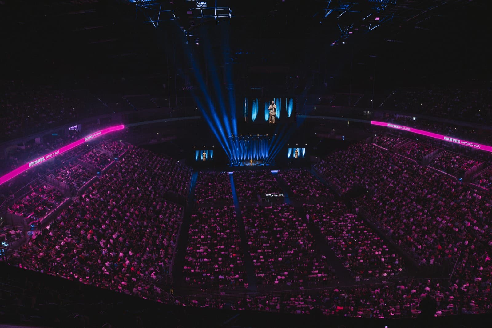 Ausverkaufte LANXESS Arena von oben, Ränge in pinkem Licht, blaue Scheinwerferkegel über der Bühne